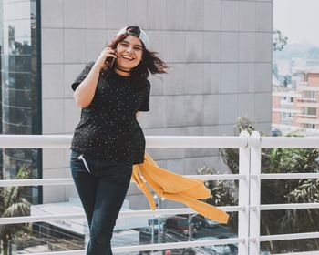 Smiling woman talking on mobile phone while standing against buildings in city