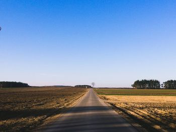 Empty road amidst field against clear blue sky