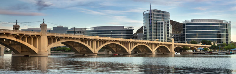 Bridge over river by buildings against sky in city