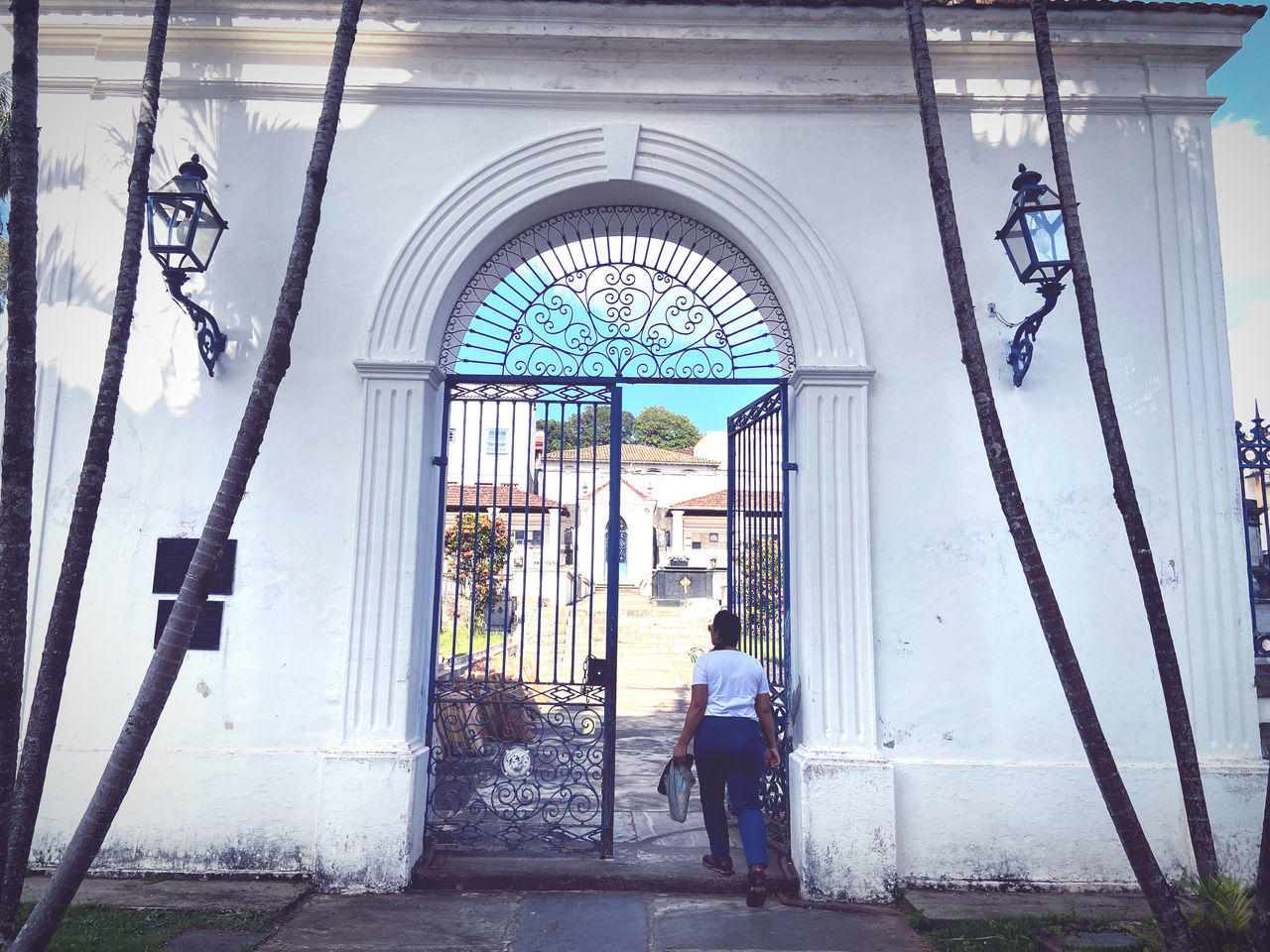 architecture, arch, full length, built structure, one person, men, day, entrance, adult, building exterior, rear view, door, urban area, walking, blue, building, standing, outdoors, lifestyles, women, gate, city, nature, casual clothing