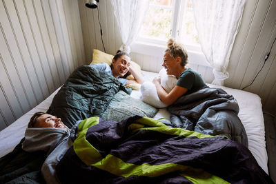 High angle view of cheerful male and female friends talking while lying on bed in cottage