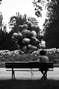 Rear view of man holding balloons while sitting on bench in park