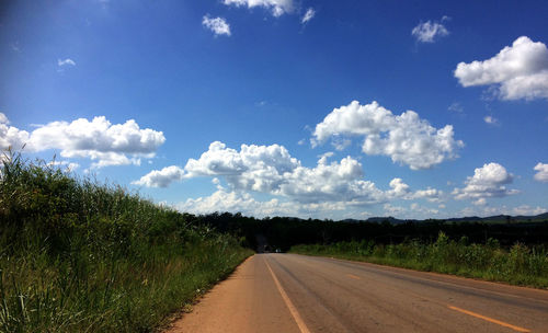 Empty road amidst field against sky