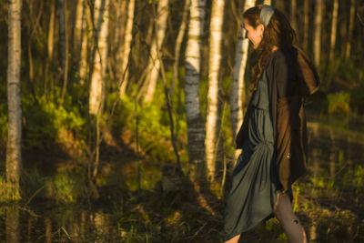 Side view of woman walking against trees at forest