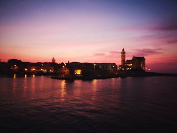 Illuminated city by river against sky during sunset