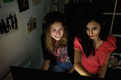 High angle view of happy teenage girl using computer with friend in darkroom at home