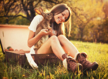 Young woman with rabbit sitting on field