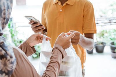 Midsection of woman receiving parcel from delivery person