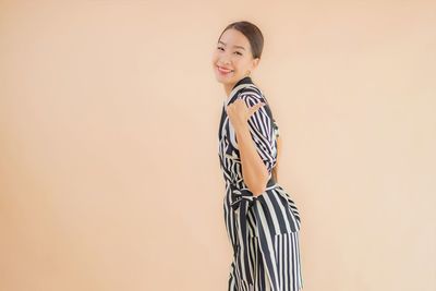 Portrait of smiling young woman standing against gray background