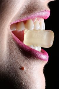 Midsection of woman holding candy through mouth against black background