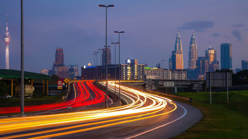 Light trails on road against buildings at dusk