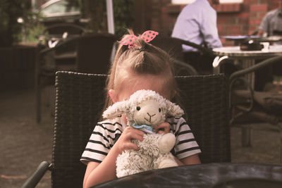 Girl covering face with toy while sitting at cafe