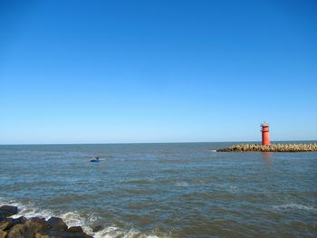 Lighthouse by sea against clear blue sky