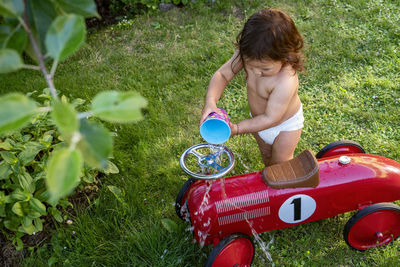 Toddler girl pouring water over ride-on car