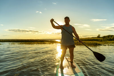 Full length of woman standing in sea against sky during sunset