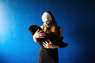 Woman wearing mask carrying stuffed toy while standing against blue wall