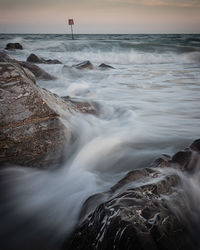 Scenic view of sea against sky during sunset with waves moving over rocks