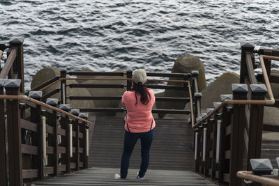 Rear view of woman standing on pier over sea