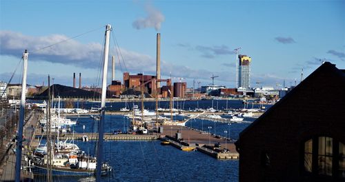 Sailboats in harbor by buildings in city against sky