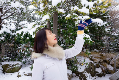 Woman standing by tree in snow