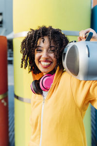 Happy woman carrying boom box on shoulder standing in front of yellow pipe