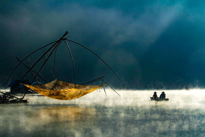 Fishermen sailing in boat by fishing net in sea against storm clouds