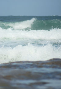 Waves rushing towards shore against sky