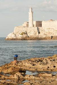 Rear view of man with fishing rod bending on rocky shore