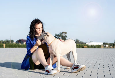 Woman with dog sitting on footpath against clear sky