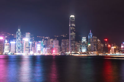 Illuminated buildings by river against sky at night