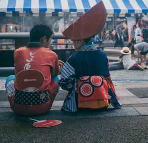 Rear view of men sitting on street in city