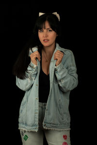 Portrait of young woman standing against black background