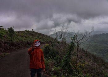 Woman on dirt road against cloudy sky