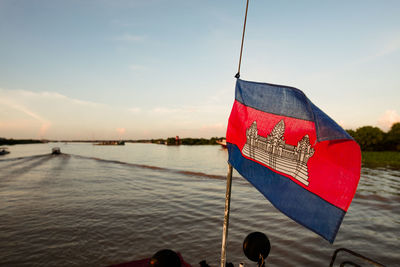 Red flag on river against sky during sunset