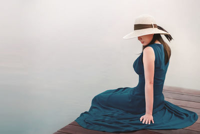 Rear view of woman sitting on jetty over lake