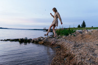Woman on the shore of the lake in a summer dress, steps on the stones
