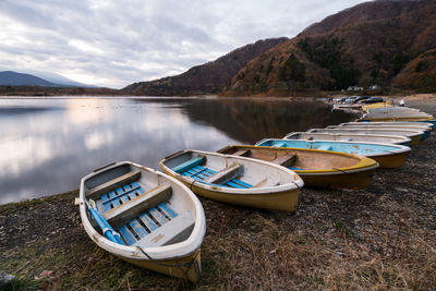 Boats moored on shore by lake against sky