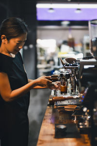 Shot in low light of female barista making a fresh coffee in cafe.
