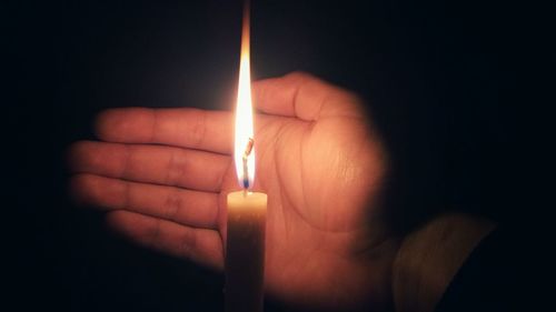 Close-up of hand covering candle