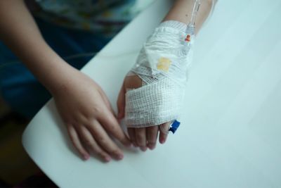 High angle view of woman with iv drip and bandage on hand sitting at clinic
