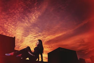 Silhouette woman sitting against orange sky