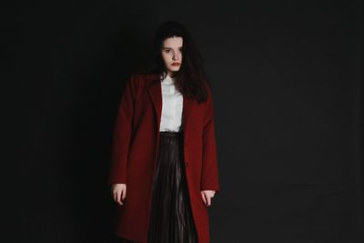 Portrait of young woman wearing red long coat against black background