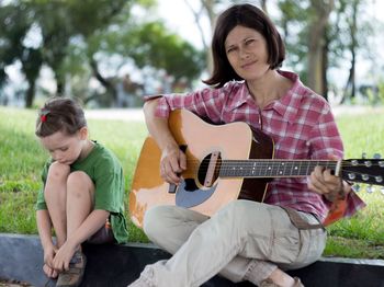 Portrait of woman playing guitar by daughter in park