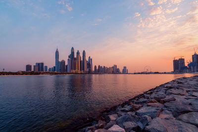 Scenic view of sea by buildings against sky during sunset