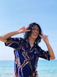 Smiling man gesturing while standing against sea and clear sky