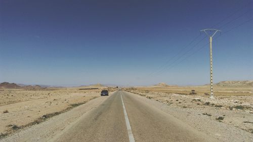 Country road at desert against clear blue sky