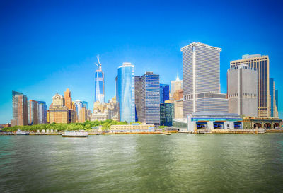 Sea by modern buildings in city against blue sky