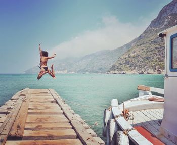 Rear view of young woman diving into sea from pier against sky