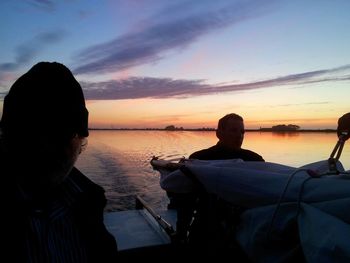 Silhouette man sitting by sea against sky during sunset