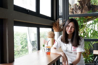 Portrait of smiling young woman standing by window